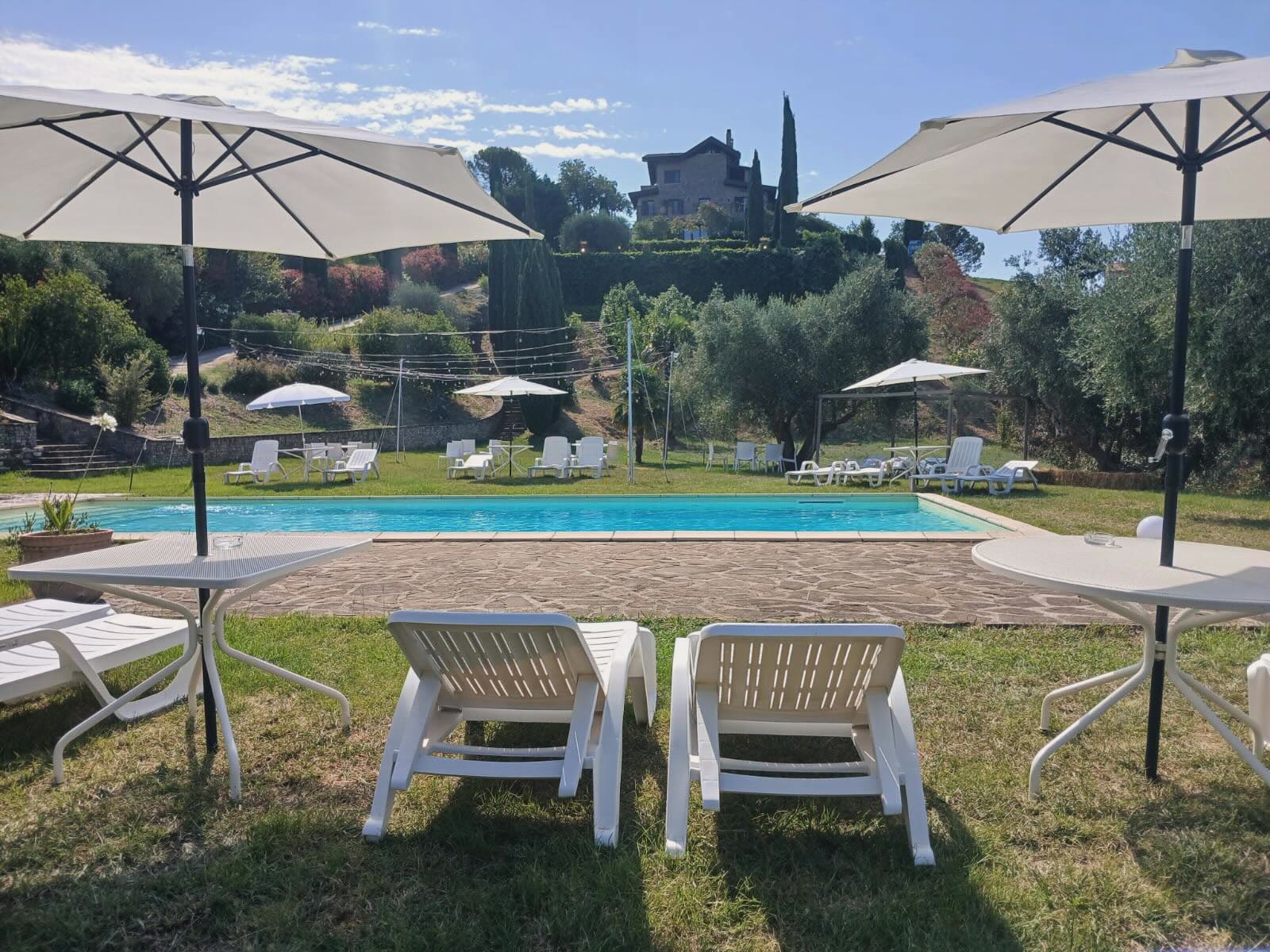 La piscina della Tenuta Torre In Pietra con il casale sulla collina, tra ulivi e cipressi