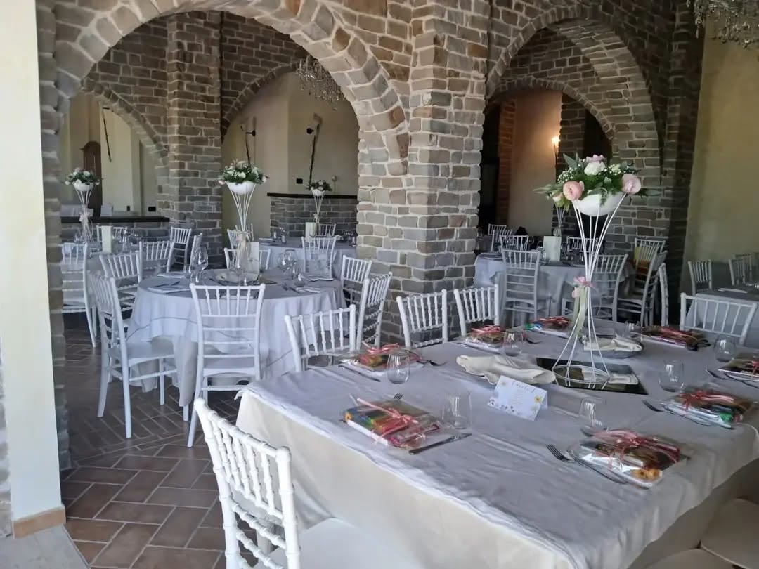 Tavoli apparecchiati per un battesimo nella sala con gli archi in pietra, con le bomboniere