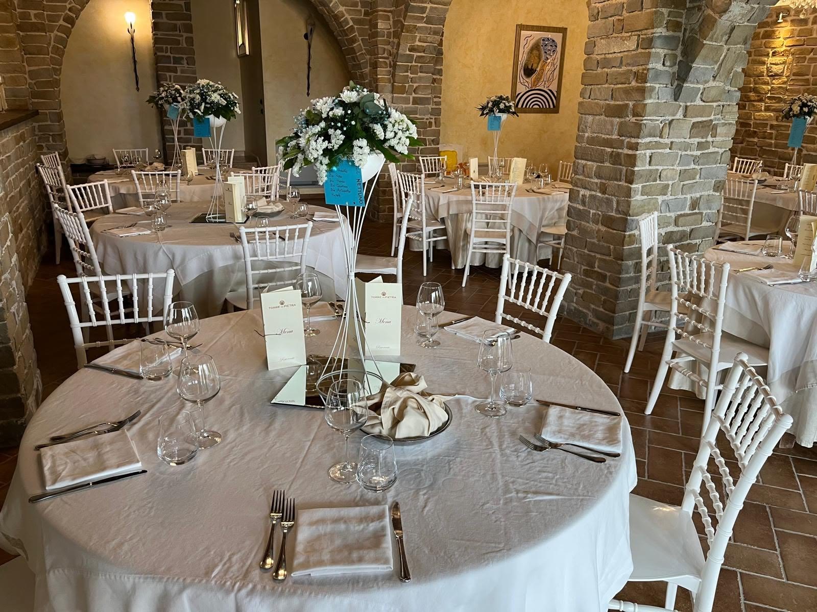 Sala interna con archi in pietra allestita per una cerimonia, tavoli rotondi e composizioni di fiori bianchi